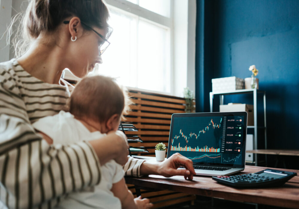 Pretty young mother with cute little baby investing in world stock market, using her laptop and online trading soft from home Pretty young mother with cute little baby investing in world stock market, using her laptop and online trading soft from home