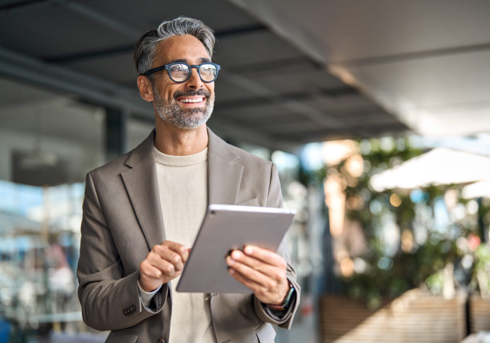 Happy middle aged professional business man executive manager using tablet. Happy elegant middle aged professional business man financial executive manager using digital tablet. Smiling confident mature businessman holding tab computer technology looking away at copy space.
